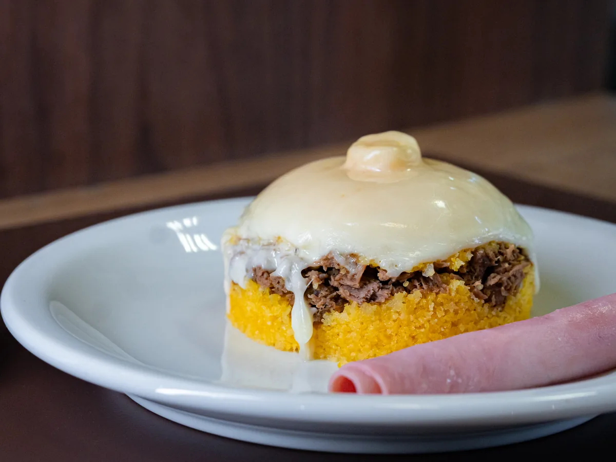 Cuscuz com carne de sol coberto de queijo derretido, servido em prato branco