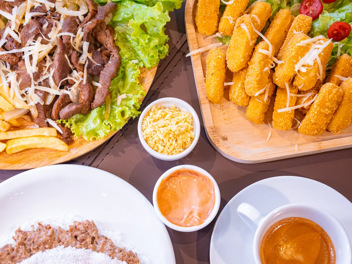 Mesa vista de cima com carne de sol, batata frita, bolinhos, tapioca e um café expresso